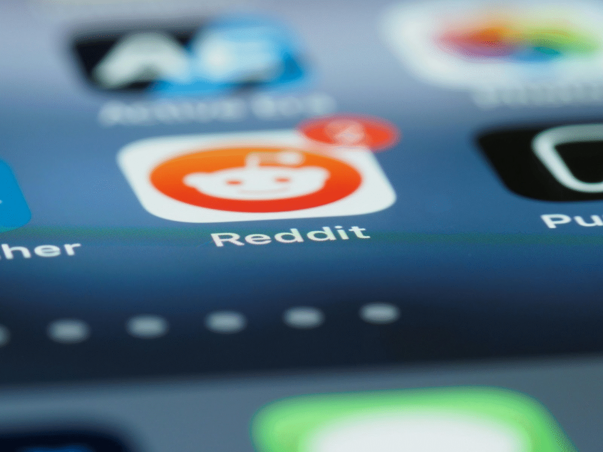 Close-up of a smartphone screen showing the Reddit app icon with a red notification bubble displaying the number 4. The app icon features Reddit's white alien logo on an orange background.