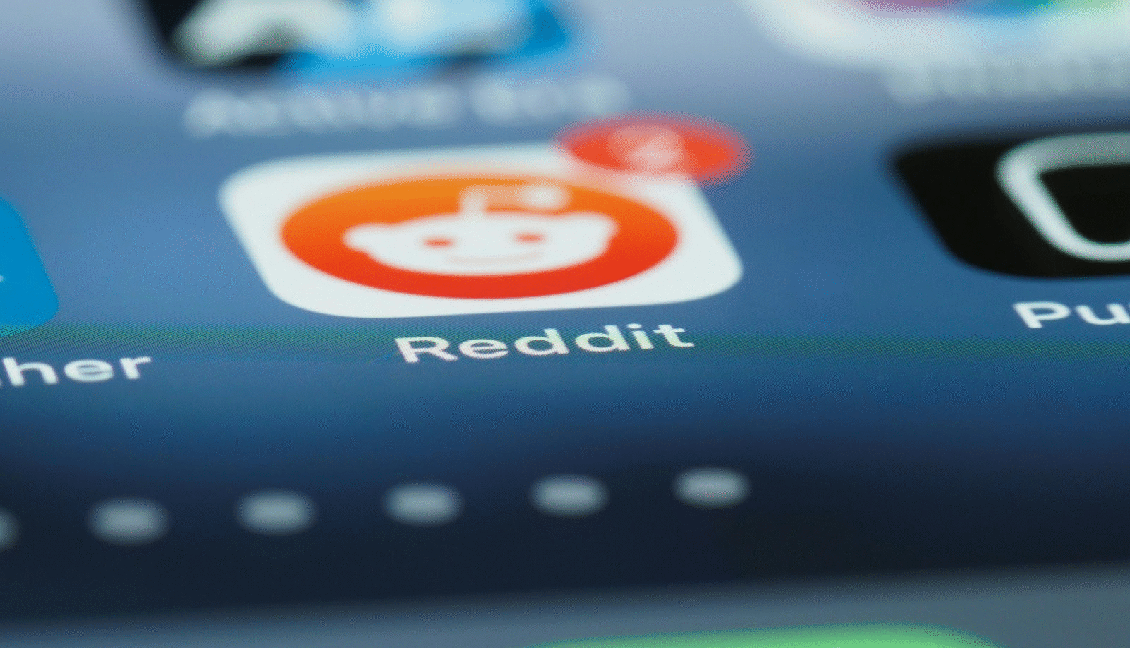 Close-up of a smartphone screen showing the Reddit app icon with a red notification bubble displaying the number 4. The app icon features Reddit's white alien logo on an orange background.