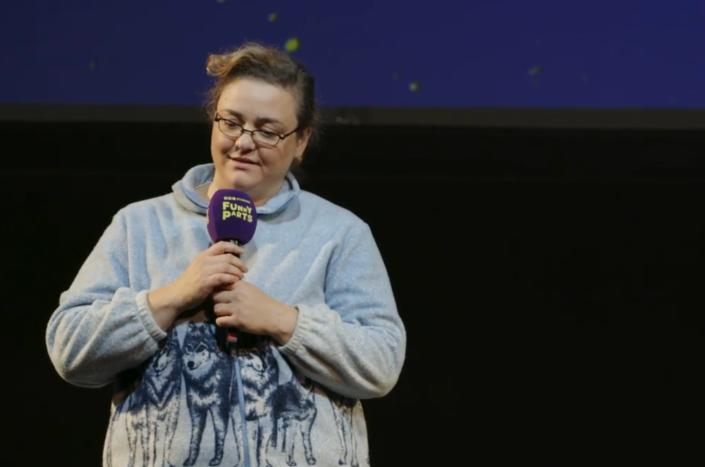 Comedian performing on stage holding a microphone, speaking during a live comedy event.