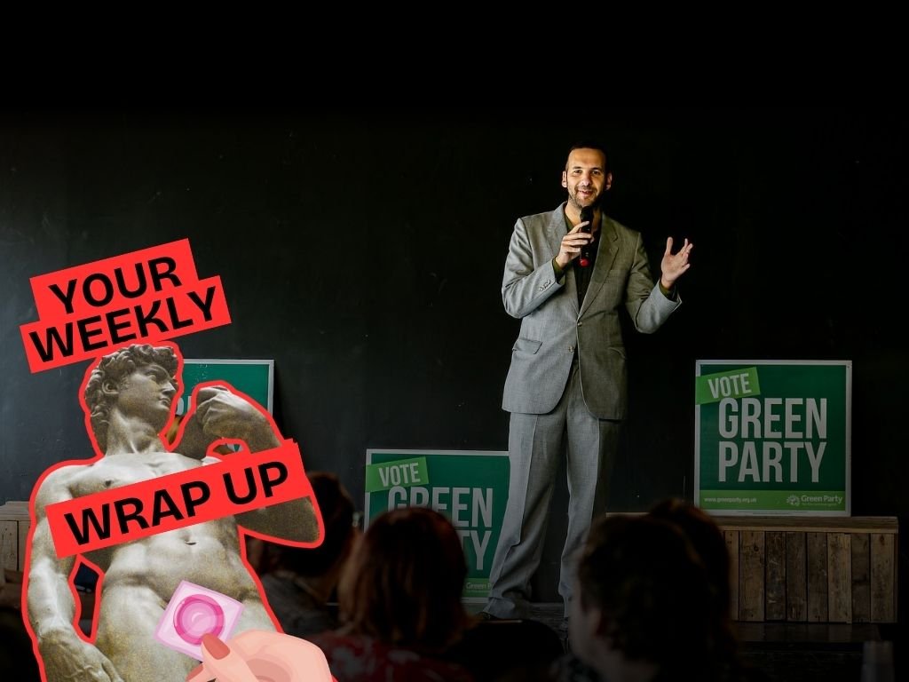 Man speaking on stage in front of “Vote Green Party” signs with audience in the foreground. Overlay graphic reads “Your Weekly Wrap Up” with a statue illustration and condom icon.