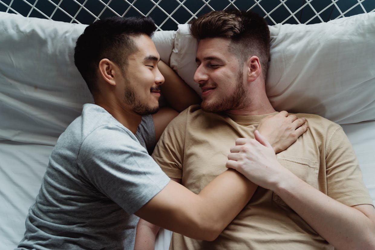 A loving interracial gay couple embracing on a bed, expressing warmth and togetherness.