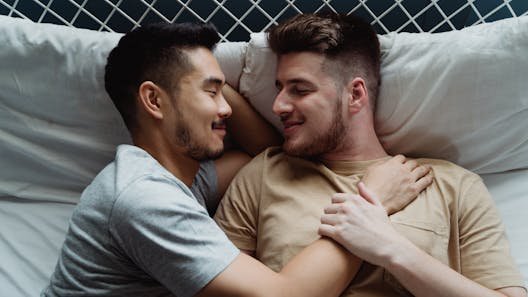 A loving interracial gay couple embracing on a bed, expressing warmth and togetherness.