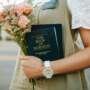 Person holding a bouquet of peach roses and a copy of The Book of Mormon, wearing a name badge and wristwatch outdoors.