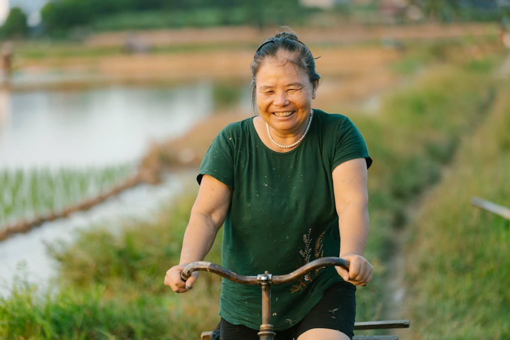 Smiling woman enjoying a bicycle ride in a lush, rural setting. Captures the essence of simple, rural life.