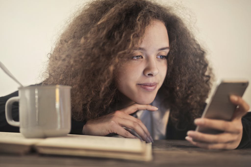 Young woman enjoying a relaxing moment while checking her smartphone indoors with a cup of coffee.