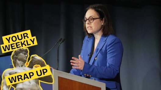 A promotional graphic for Pillow Talk Scotland's "Your Weekly Wrap Up." The background shows a woman in a bright blue blazer speaking at a lectern with microphones, gesturing as she addresses an audience. In the bottom left corner is the recurring "Your Weekly Wrap Up" branding featuring Michelangelo's David statue holding a condom packet, with yellow labels reading "YOUR WEEKLY" and "WRAP UP."