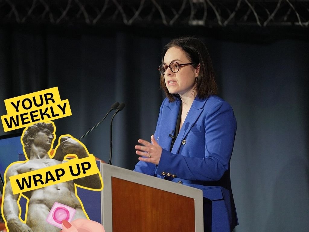 A promotional graphic for Pillow Talk Scotland's "Your Weekly Wrap Up." The background shows a woman in a bright blue blazer speaking at a lectern with microphones, gesturing as she addresses an audience. In the bottom left corner is the recurring "Your Weekly Wrap Up" branding featuring Michelangelo's David statue holding a condom packet, with yellow labels reading "YOUR WEEKLY" and "WRAP UP."