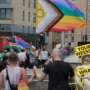A crowd marches through Glasgow during a Pride event, with people carrying rainbow, Progress Pride, bisexual and Palestinian flags. In the foreground, two people walk hand in hand beneath a large Progress Pride flag. Overlaid on the image is Pillow Talk Scotland's "Your Weekly Wrap Up" graphic featuring Michelangelo's David statue, bold yellow text and a pink condom illustration.