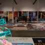 A large exhibition space filled with sections of the UK AIDS Memorial Quilt displayed across the floor and hanging on the walls, with visitors walking among them. A “Your Weekly Wrap Up” graphic appears in the lower-left corner.