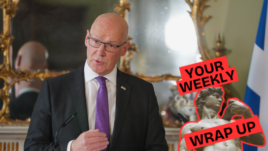 A bald man in glasses, a dark suit and purple tie speaks at a lectern beside a Scottish flag, with an ornate mirror behind him. A “Your Weekly Wrap Up” graphic with a classical statue and condom illustration appears on the right.